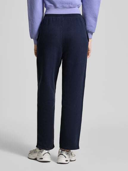 Frauenmodel trägt Sweatpants mit Label-Print Modell 'PLIZZY' von American Vintage aus reiner Baumwolle im Relaxed-Fit, Farbe Dunkelblau, elastischer Bund, Ganzkörperansicht Rückansicht.