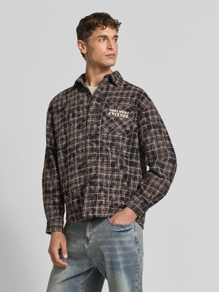 Männermodel trägt Regular Fit Freizeithemd mit Label-Print von Don't Waste Culture, braun-schwarz kariert, reine Baumwolle, Nahaufnahme Oberkörper. Rückenlänge, Schulterbreite und Ärmellänge bei Größe M, Kentkragen, Brusttasche mit Label-Print.