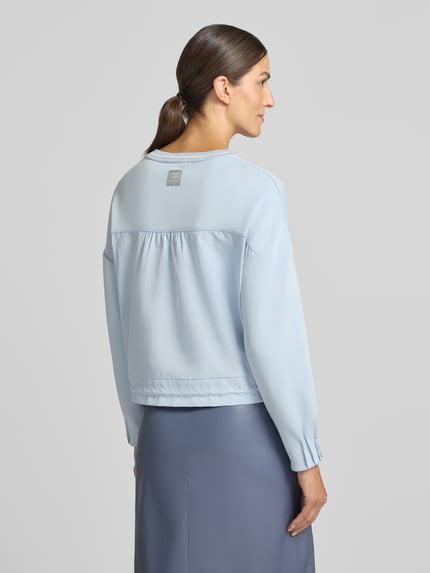 Frauenmodel trägt Sweatshirt aus Viskose-Mix von Marc Cain in hellblau, lockere Passform, Strickbesatz mit Streifenmuster, Tunnelzug am Bund, gerippter Rundhalsausschnitt, Ganzkörperansicht Rückansicht.