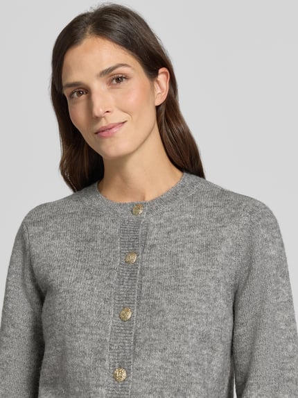 Frauenmodel trägt Strickjacke mit Zierknöpfen Modell 'VMHAZEL' von VERO MODA in meliertem Grau mit Rundhalsausschnitt, Nahaufnahme Oberkörper.