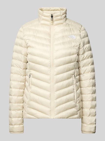 Produktfoto, cremefarbene Steppjacke mit Stehkragen und Label-Stitching von The North Face, glatte Oberfläche, sichtbare Reißverschlüsse, Regular Fit