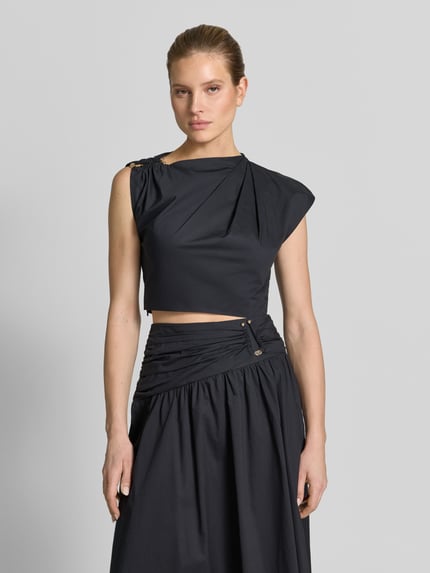 Vrouwenmodel draagt Cropped blouse in asymmetrisch design model 'Dottie' van Forever New van puur katoen met plooien en siergarnering, korte fit, mouwloos, ruglengte maat 36: 39 cm, effen zwart, gladde structuur, Ganzkörperansicht van voren.