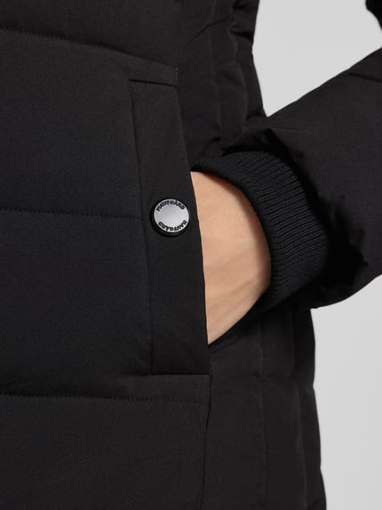 Frauenmodel trägt Steppmantel mit Zweiwege-Reißverschluss von NAUTGÅRD 'ECLIPSE', schwarz, glatte Struktur, Detailaufnahme, Kontext: Damen Steppmantel von NAUTGÅRD, Slim Fit, Kapuze mit Kunstfell, Modell 'ECLIPSE', Rückenlänge 115 cm, Schulterbreite 40 cm, Brustweite 46 cm, Ärmellänge 65 cm.