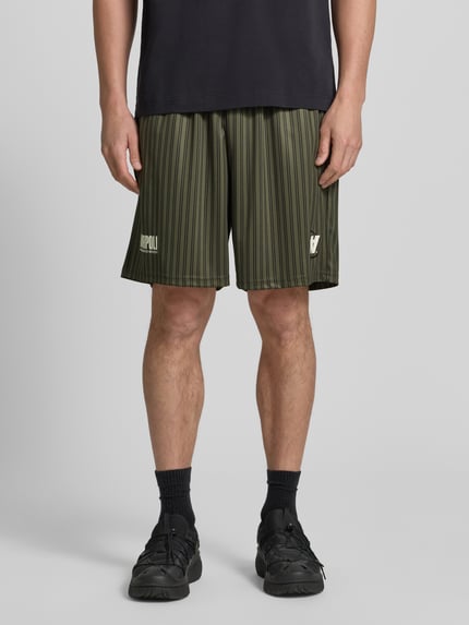 Mężczyzna nosi Regular Fit Shorts mit Label-Print Modell 'Lama' od Wood Wood w oliwkowo-czarne paski, elastischer bund, Szerokość w rozmiarze M: 40 cm, długość nogawki wewnętrznej: 19 cm, Ganzkörperansicht von vorne