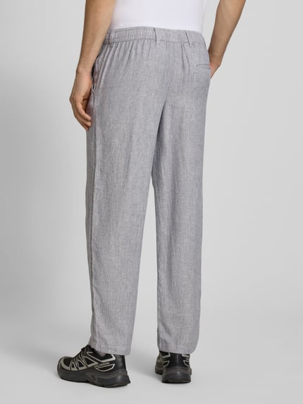 Mężczyzna nosi Leinenhose mit Bindegürtel Modell 'KARL MYKONOS' od Jack & Jones, szary melanż, krój relaxed fit, francuskie kieszenie, materiał len-wiskoza, kieszeń z tyłu, szerokość w rozmiarze M: 41 cm, długość nogawki: 78 cm, widok całej sylwetki z tyłu.