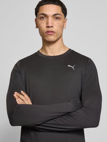 Męski model nosi bluzkę z długim rękawem Longsleeve mit Logo Modell 'CLOUDSPUN' od PUMA PERFORMANCE, czarny, mieszanka materiałów z dodatkiem streczu, krój regular fit, okrągły dekolt, logo, długość tyłu w rozmiarze M: 66 cm, zbliżenie na górną część ciała
