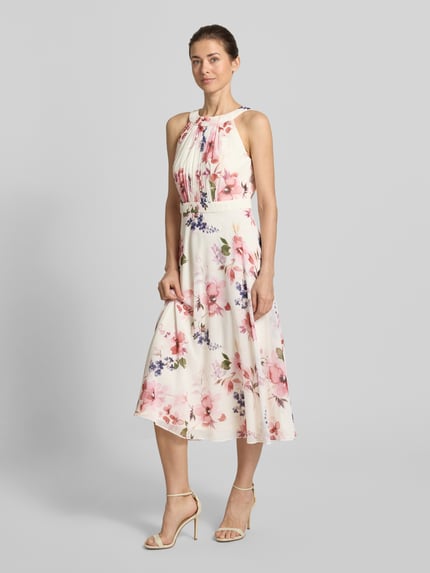Frauenmodel trägt Midikleid mit floralem Allover-Print von Christian Berg Cocktail in Weiß mit Rosa, Taillierte Passform, Rundhalsausschnitt, Gelegte Falten, Ärmelloses-Design, Nahtreißverschluss, fließender Stoff, Ganzkörperansicht von vorne.