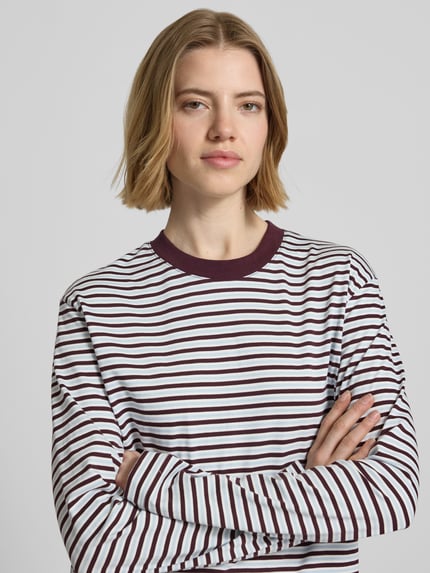 Kobiece model nosi bluzkę z długim rękawem Boxy Fit Longsleeve model 'SOPHIA' od JJXX z bawełny, wzór w paski, okrągły dekolt, długość tyłu w rozmiarze S: 53 cm, zbliżenie na górną część ciała z przodu.