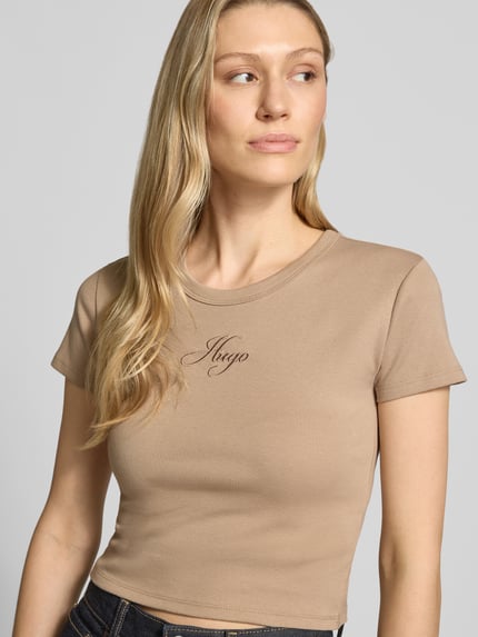 Frauenmodel trägt Slim Fit T-Shirt aus Baumwoll-Mix Modell 'DELANOR' von HUGO in Optik: Unifarben mit Label-Stitching-Applikation, Rundhals, Kurzarm, Materialverarbeitung: Jersey, Nahaufnahme Oberkörper.