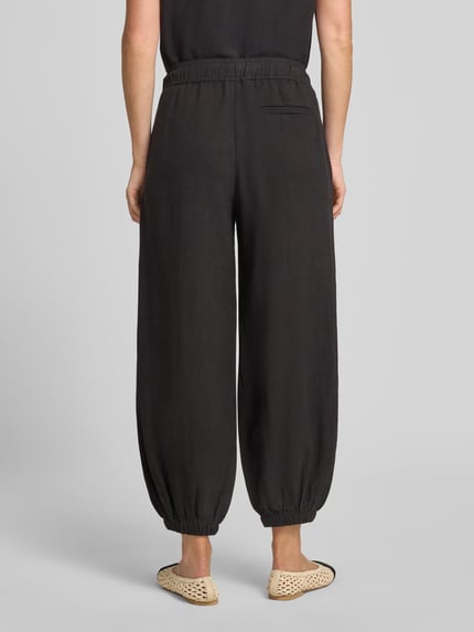 Frauenmodel trägt Relaxed Fit Hose aus Viskose-Mix Modell 'Myha' von OPUS in Schwarz mit elastischem Bund, Eingrifftaschen, verkürzter Passform, elastischen Beinabschlüssen und Leinen-Anteil, Ganzkörperansicht Rückansicht.