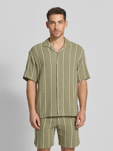 Männermodel trägt Regular Fit Freizeithemd mit Streifenmuster von MCNEAL aus reiner Bio-Baumwolle, grün-beige, Reverskragen, Knopfleiste, Ganzkörperansicht von vorne.