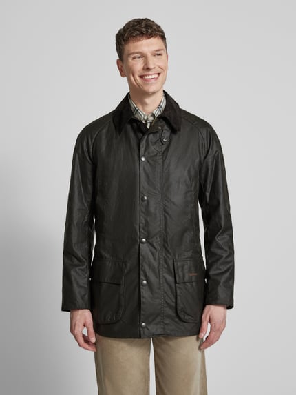 Męski model nosi Original Wachsjacke od Barbour, woskowana powierzchnia, całkowicie z ociepleniem, klasyczny sztruksowy kołnierz, nakładane kieszenie z zatrzaskami, widok na cały przód.