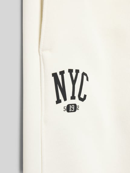 Produktfoto, Stoffhose mit elastischem Bund von CHAMPION in Creme, Label-Print NYC, Baumwoll-Mix, glatte Textur, französische Eingrifftaschen