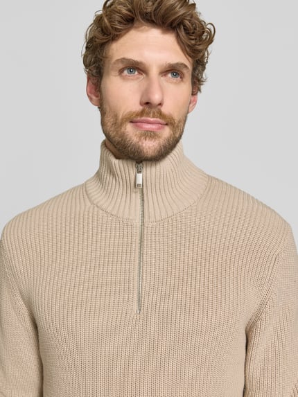 Männermodel trägt Slim Fit Strickpullover aus reiner Baumwolle mit Troyer-Kragen von MCNEAL, beige, gerippte Textur, Nahaufnahme Oberkörper.
