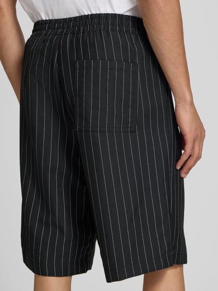 Mężczyzna nosi szorty z elastycznym pasem model 'CRISTIANO' od Redefined Rebel, mieszanka materiałów z dodatkiem streczu, krój relaxed fit, szerokość w rozmiarze M: 42 cm, długość wewnętrzna nogawki: 27 cm, widok tyłu w ujęciu całopostaciowym.