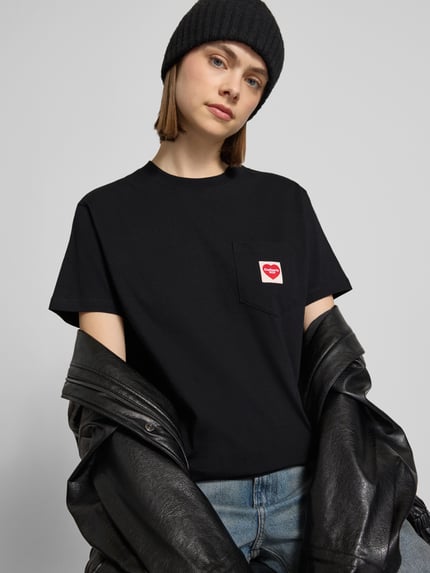 Frauenmodel trägt T-Shirt mit Label-Patch von Carhartt Work In Progress, Schwarz, Reine Baumwolle, Gerader-Schnitt, Rundhalsausschnitt, Brusttasche, Rückenlänge bei Größe S: 58 cm, Nahaufnahme Oberkörper.