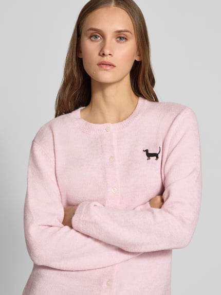 Kobiece model nosi jasnoróżowy kardigan rozpinany z okrągłym dekoltem Regular Fit Strickjacke mit Rundhalsausschnitt Modell 'EVIA' od ONLY, damski kardigan z ONLY, zbliżenie na górną część ciała.