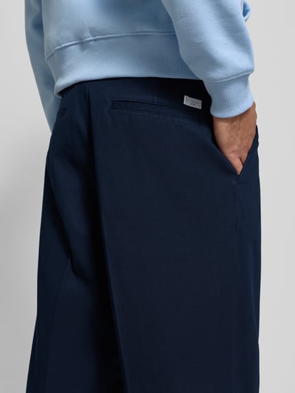 Männermodel draagt Weite Fit Hose aus reiner Baumwolle Modell 'MURRAY' van Tommy Hilfiger, donkerblauw, detailaufnahme heup en zak, unikleur, label patch, logo-detail, wijd model, herenmode.