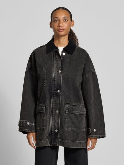 Frauenmodel trägt Oversized Jeansjacke aus reiner Baumwolle von ARMEDANGELS in dunklem Denim, große Taschen, silberne Knöpfe, Ganzkörperansicht von vorne.