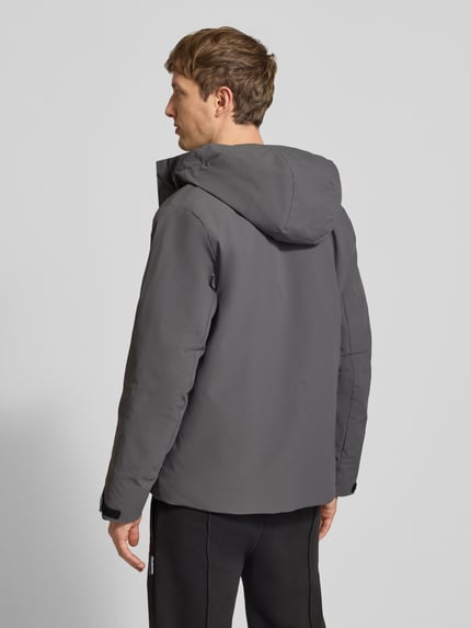 Mężczyzna model nosi kurtkę z kapturem Jacke mit verdecktem Reißverschluss Modell 'KEEN' od JACK & JONES, krój regular fit, Patki przy mankietach, Długość tyłu w rozmiarze M: 72 cm, Szerokość ramion w rozmiarze M: 49 cm, Szerokość klatki piersiowej w rozmiarze M: 60 cm, Długość rękawów w rozmiarze M: 68 cm, gładki odcień szarości, duża powierzchnia matowa, całkowity widok z tyłu.