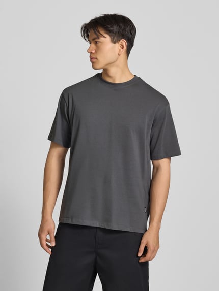 Męski model nosi męski t-shirt Oversized T-Shirt Modell 'FISHER' von Blend z bawełny, okrągły dekolt, ciemnoszary kolor, długość tyłu w rozmiarze M: 72 cm, całkowity widok od przodu.