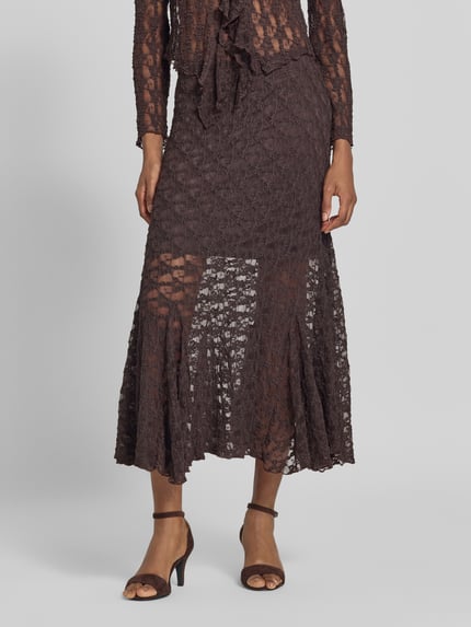 Vrouwenmodel draagt midirok met florale kant Model 'Reddy' van FREE/QUENT, elastische materiaalmix, flared fit, totale lengte 90 cm, bandwijdte maat S 37 cm, donkere bruine tint, textuurrijk oppervlak, detailopname onderlichaam, voorkant.