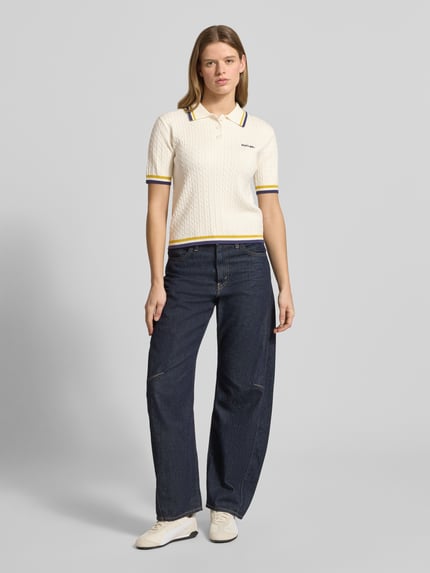 Frauenmodel trägt Regular Fit Poloshirt mit Zopfmuster und Logo-Stitching von Karo Kauer aus Viskose-Mix, Polokragen, kurze Knopfleiste, cremefarben mit gelben und blauen Streifendetails, Struktur durch Zopfmuster, Rückenlänge 52 cm, Ärmellänge 23 cm, Ganzkörperansicht von vorne.