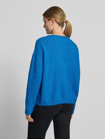 Frauenmodel trägt Relaxed Fit Strickjacke aus Woll-Mix mit Leinen-Anteil von American Vintage in Blau, gerippte Bündchen, Rückenansicht, Damen Strickjacke, Ganzkörperansicht Rückansicht.