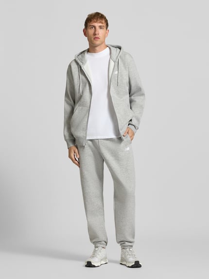 Männermodel trägt Regular Fit Sweatpants aus Baumwoll-Mix mit Label-Stitching von New Balance in Hellgrau, Ganzkörperansicht von vorne. Herren Sweatpants, elastischer Bund mit Tunnelzug, Innenbeinlänge Größe M 79 cm.