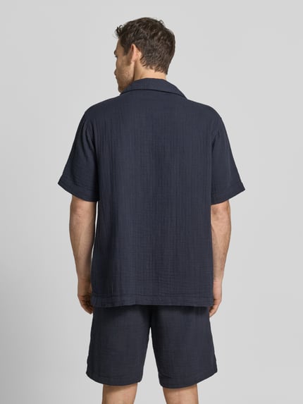 Męski model nosi Relaxed Fit Freizeithemd mit Strukturmuster von Lindbergh, bawełna, krój relaxed fit, kołnierz z połami, krótki rękaw, listwa guzikowa, długość tyłu w rozmiarze M: 80 cm, szerokość ramion w rozmiarze M: 47 cm, długość rękawów w rozmiarze M: 29 cm, fakturowany wzór, widok całej sylwetki z tyłu.