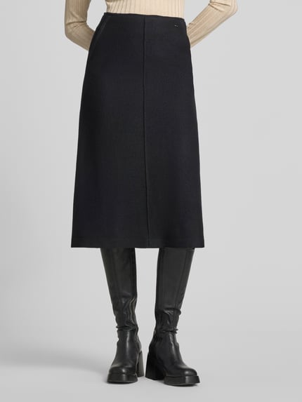Frauenmodel trägt Midirock aus Schurwolle mit Reißverschluss von Marc Cain in Schwarz, A-Linie, Label-Detail, Ganzkörperansicht von vorne.