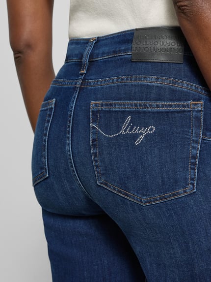 Vrouwenmodel draagt Flared Fit Jeans uit elastische katoenmix van Liu Jo White in donkerblauw met 5-pocketmodel en riemlussen, detailopname achterkant. Context: Dames jeans, knoop- en ritssluiting, bandwijdte maat 27: 36 cm, binnenbeenlengte maat 27: 77 cm.