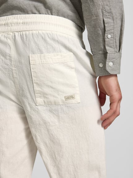 Männermodel trägt Hose aus Baumwoll-Leinen-Mix mit elastischem Bund von Blend, cremefarben, sichtbare Textur, Detailaufnahme Rückansicht. Herren Regular-Fit Modell 'ABAN', Bundweite 39 cm, Innenbeinlänge 76 cm, Hosentasche und Label.