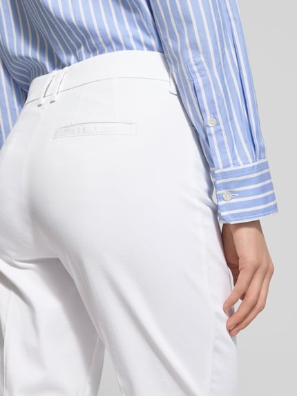 Frauenmodel trägt weiße Straight Fit Stoffhose mit Lyocell-Anteil Modell 'Mara' von BRAX, glatte Struktur, Detailaufnahme Gesäßtasche, Nahaufnahme Rückansicht. Elastischer Baumwoll-Mix, Bügelfalten, verkürzte Passform, Eingriff- und Gesäßtaschen, Knopf- und Reißverschluss, Bundweite Größe 36: 39 cm, Innenbeinlänge Größe 36: 68 cm.