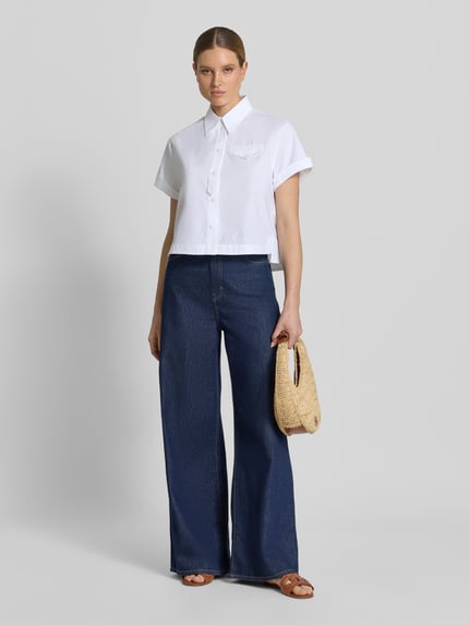 Vrouwenmodel draagt Boxy Fit Bluse mit Brusttasche van Luisa Cerano in witte katoen met borstzak, knoopsluiting, omgeslagen mouw, hemdkraag; gecombineerd met donkerblauwe broek, vooraanzicht volledige lichaamslengte.