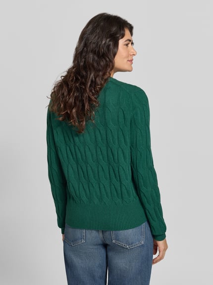 Frauenmodel trägt grüne Strickjacke aus Wolle mit Logo-Detail von Tommy Hilfiger im Zopfmuster, gerippte Abschlüsse, Ganzkörperansicht Rückansicht.