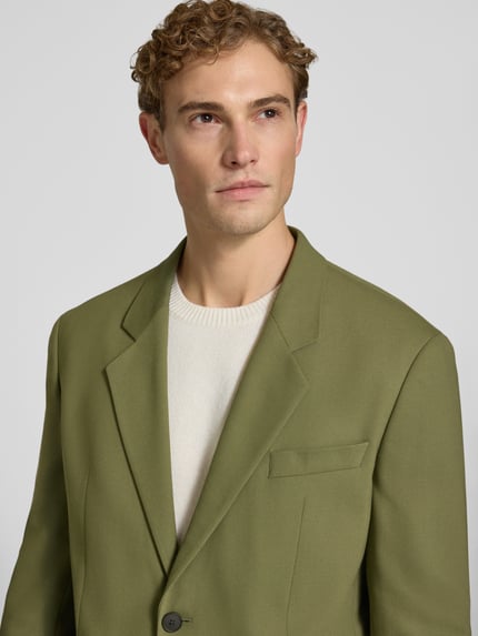 Männermodel trägt Regular Fit Sakko mit Viskose-Anteil Modell 'Karlo243X' von HUGO in Olivgrün, glatte Oberfläche, Nahaufnahme Oberkörper.