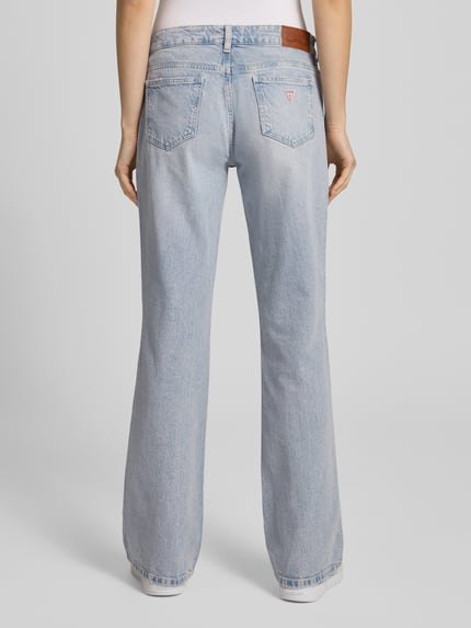 Frauenmodel trägt Bootcut Jeans im Used-Look von Guess Jeans in hellblauem Baumwoll-Elasthan-Mix mit Label-Detail, Ganzkörperansicht Rückansicht.