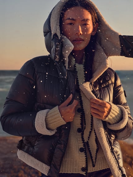 Frauenmodel trägt Steppjacke mit Stehkragen und Riegeln Modell 'NESSIE2' von khujo mit Teddyfell-Futter, Kapuze, Eingrifftaschen, Regular Fit; Rückenlänge 51 cm, Schulterbreite 45 cm, Brustweite 47 cm, Ärmellänge 54 cm, Ganzkörperansicht von vorne.