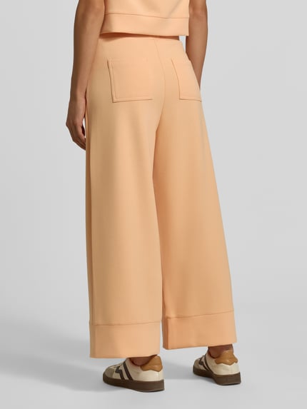 Frauenmodel trägt Wide Leg Sweatpants aus Modal-Mix von Rich & Royal in Pfirsichfarbe mit Bundfalten und Gesäßtaschen, Ganzkörperansicht Rückansicht.