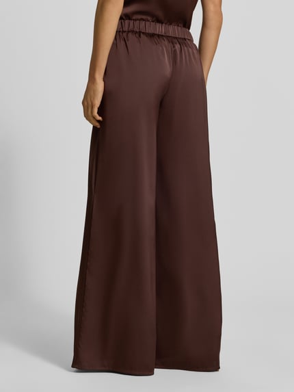 Frauenmodel trägt Wide Fit Stoffhose aus Satin von VM by Vera Mont in Braun mit teilelastischem Bund, Bundfalten, Ganzkörperansicht Rückansicht.