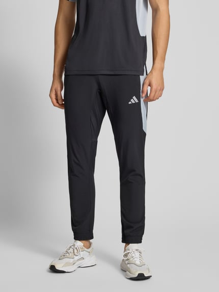 Männermodel trägt Slim Fit Trainingshose mit Logo-Print Modell 'Tech' von adidas Training, Elastischer-Material-Mix, Nahaufnahme Oberkörper.