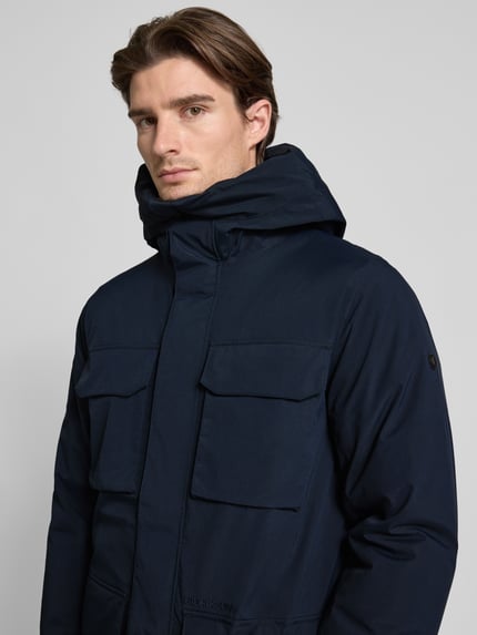 Männermodel trägt Herren Parka mit Kapuze und Pattentaschen Modell 'AIDEN' von Didriksons, Regular-Fit, Nahaufnahme Oberkörper. Rückenlänge bei Größe M: 92 cm, Schulterbreite: 47 cm, Brustweite: 56 cm, Ärmellänge: 69 cm.