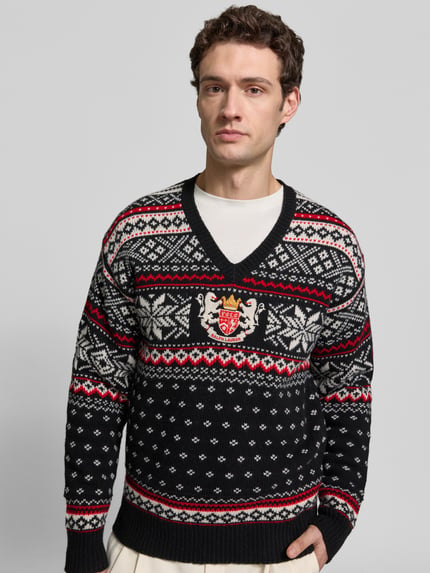 Männermodel trägt Pullover aus Wolle mit Wappenstickerei von POLO RALPH LAUREN in Strickoptik mit Rauten- und Sternenmuster, Nahaufnahme Oberkörper.