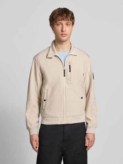 Männermodel trägt Regular Fit Bomberjacke mit Stehkragen Modell 'Parker' von Jack & Jones in Beige, Softshell, Vorderansicht, Ganzkörperansicht von vorne. Zu sehen sind Napoleontasche, Druckknopf-Eingrifftaschen, elastische Abschlüsse, Maße M: Rückenlänge 67 cm, Schulterbreite 43 cm, Brustweite 55 cm, Ärmellänge 65 cm.