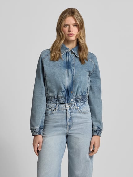 Frauenmodel trägt Relaxed Fit Jeans-Bomberjacke aus Baumwoll-Mix von Hugo Blue in Denim-Optik mit Umlegekragen und verdecktem Reißverschluss, Ganzkörperansicht von vorne.