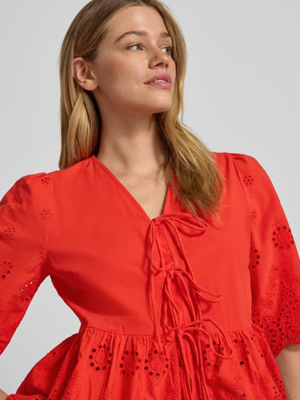Kobiece model nosi bluzkę Regular Fit Bluse mit Lochstickereien Modell 'Cornelia' od YAS, haft angielski, krój regular fit, dekolt w serek, rękaw o dł. 1/2, ozdobna kokarda, długość tyłu w rozmiarze 36: 56 cm, długość rękawów w rozmiarze 36: 37 cm, intensywny czerwony kolor, gładka i ażurowa faktura, detaliczna faktura haftu, nahaufnahme górnej części ciała.