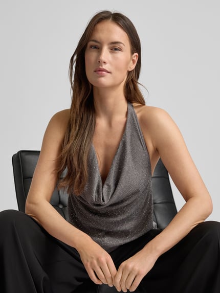 Frauenmodel trägt Blusentop mit Viskose-Anteil Modell 'SPARKLE' von Mango, silberfarbene Strassstein-Optik, Neckholder, Nahaufnahme Oberkörper.