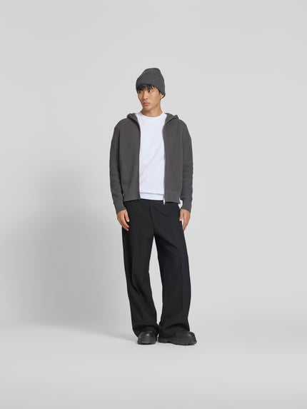 Męski model nosi Regular Fit Jacke in Strick-Optik od WON HUNDRED, szara dzianinowa kurtka z bawełny, kaptur, dwukierunkowy zamek, długość tyłu w rozmiarze M 68 cm, szerokość w rozmiarze M 46 cm, długość rękawa w rozmiarze M 72 cm, przód w pełnym wymiarze