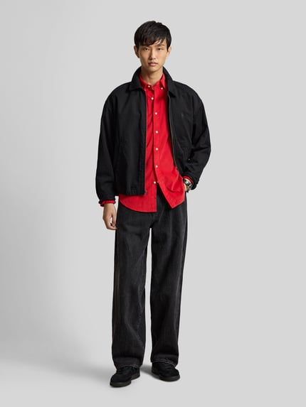 Männermodel trägt Custom Fit Freizeithemd aus reiner Baumwolle von Polo Ralph Lauren in Rot, dazu schwarze Hose und Jacke, Ganzkörperansicht von vorne.